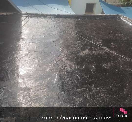 גג אטום בזפת שחורה מבריקה בשמש